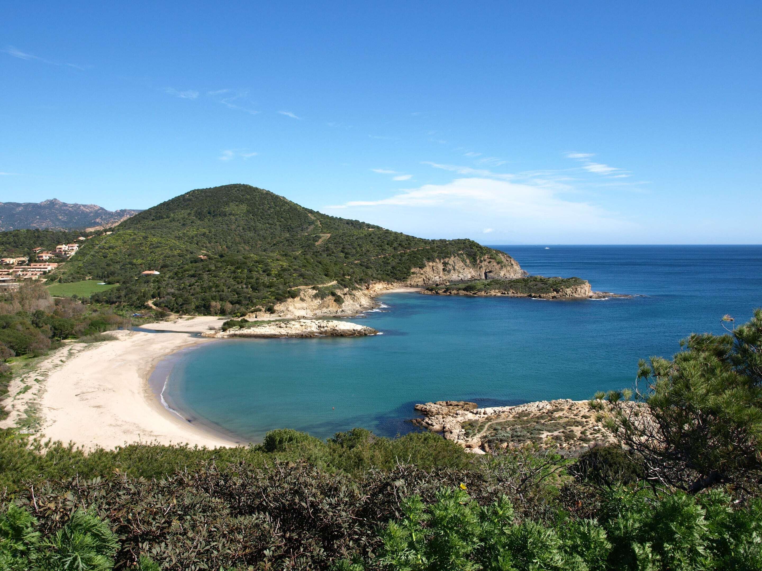 Eine Küstenlandschaft mit Strand, Felsenformationen und einem bewachsenen Hügel.