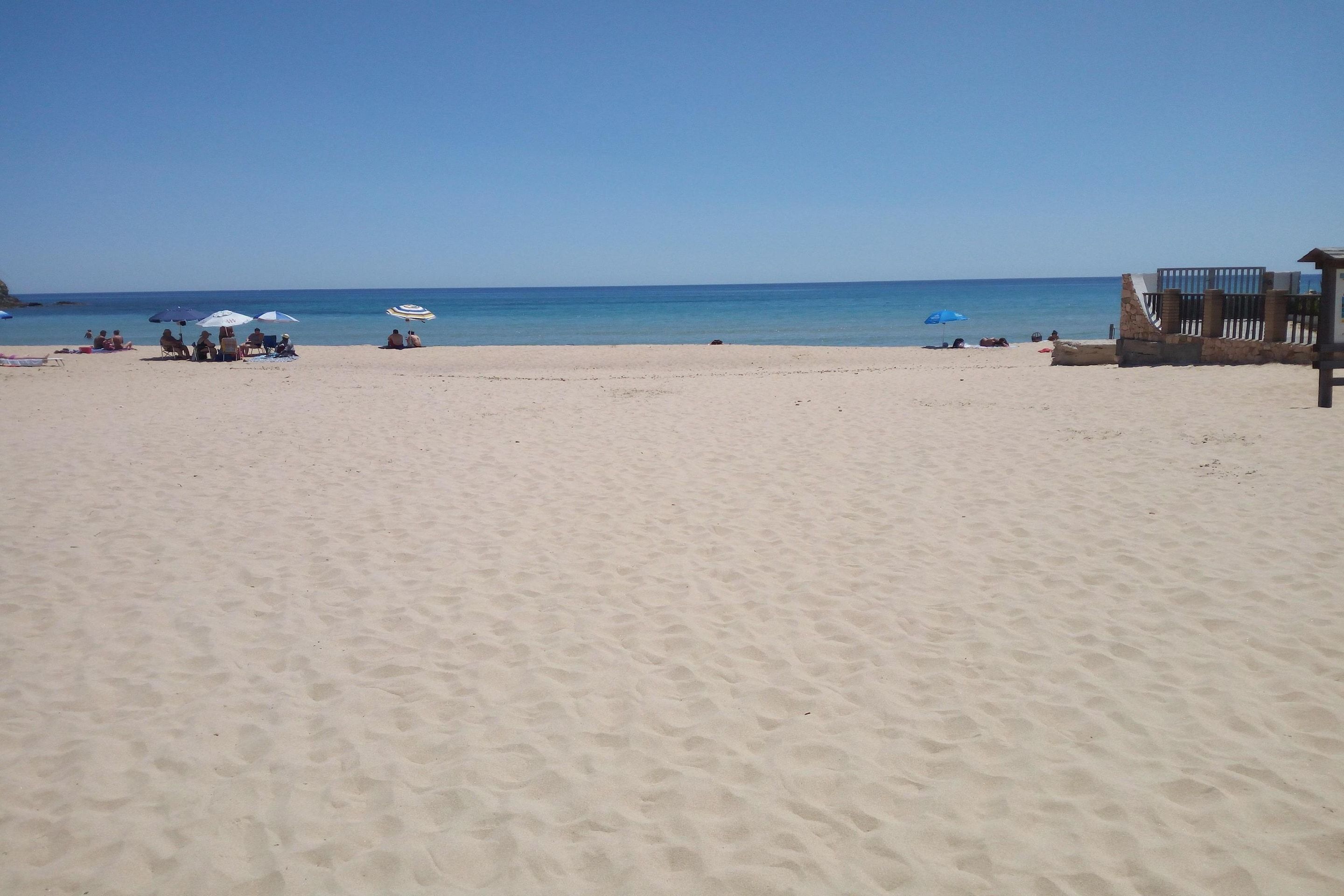 A beach with a few umbrellas and people.
