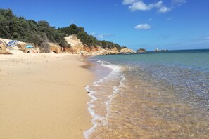 Una playa con agua cristalina, orilla de arena y acantilados rocosos.