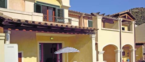 Un bâtiment à deux étages doté d’un balcon, d’un espace extérieur aménagé avec des chaises et un parasol, et d’un appareil de climatisation visible.