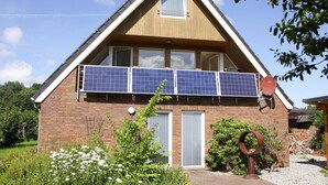 Een twee verdiepingen tellend huis met een schuin dak, zonnepanelen op de tweede verdieping, een klein raam en een deur.