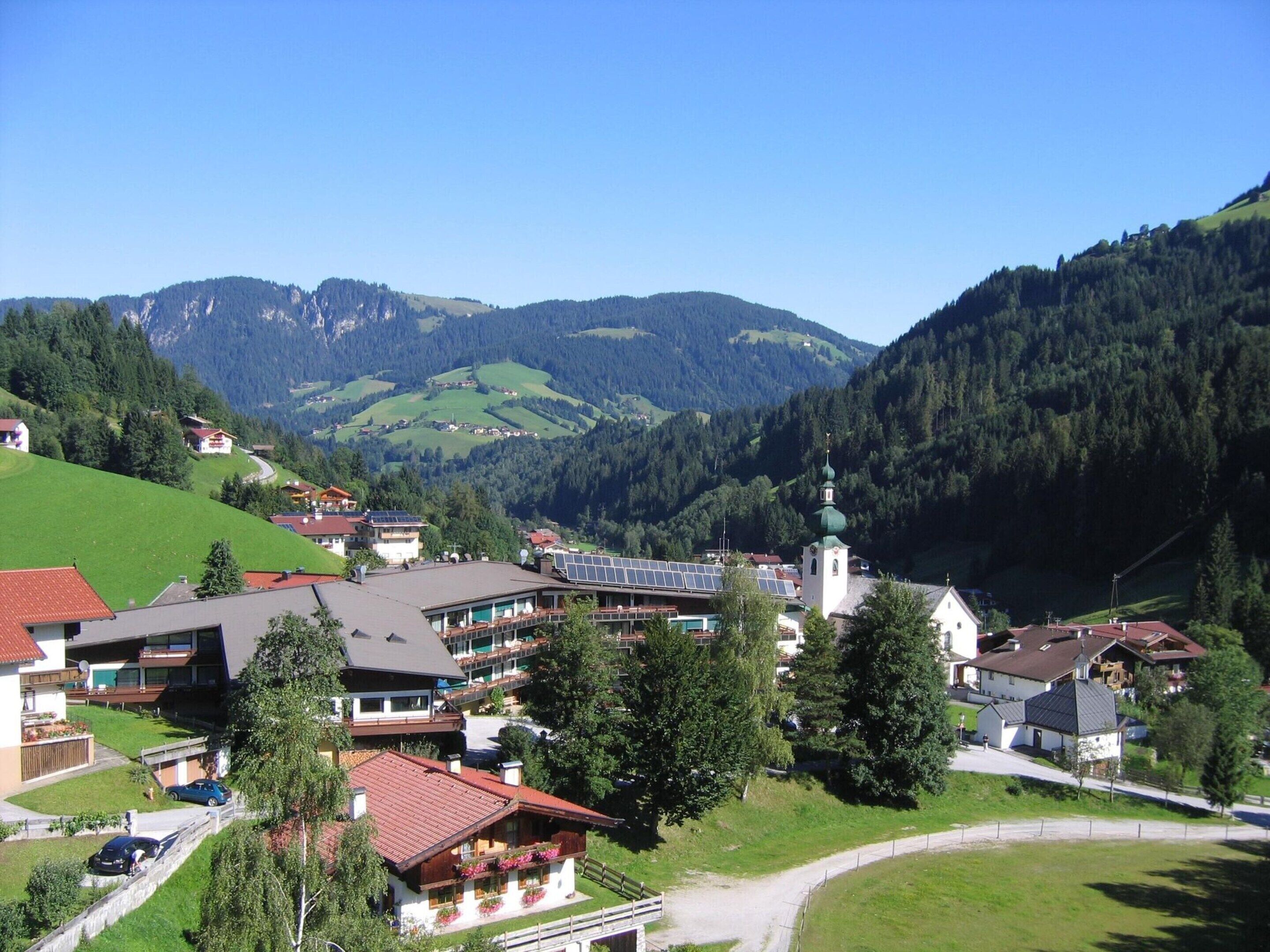 A mountain village with traditional houses, a church, and a view of the surrounding hills.