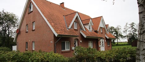 A red brick house with a steeply pitched roof, multiple chimneys, and a small porch area.