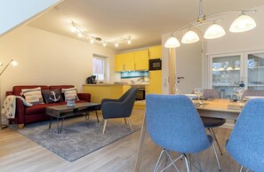 A modern living space with a red sofa, a dining table with chairs, and a kitchen area with yellow cabinets. - Ferienwohnung in St. Peter-ording (St. Peter-Ording)