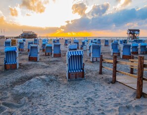 A beach with rows of striped beach chairs and a wooden pier. - Ferienwohnung in St. Peter-ording (St. Peter-Ording)