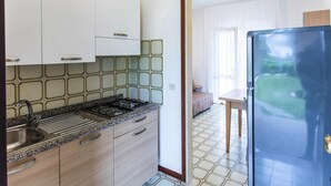 A kitchen with white cabinets, a gas stove, and a sink. There is a dining area with a table and chairs. - Apartment in Italy Near Sandy Beach (San Michele al Tagliamento)