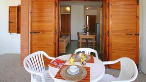 A dining area with a table set for two, a chair, and a small table with a bottle and a cup. - Apartment in Italy Near Sandy Beach (San Michele al Tagliamento)