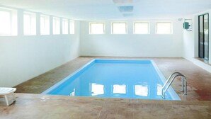 Una piscina interior rectangular con suelo de baldosas y una escalera de metal.