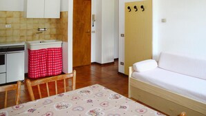 Una habitación pequeña y funcional con kitchenette, una cama individual, una mesa con mantel estampado y una puerta con cerradura.