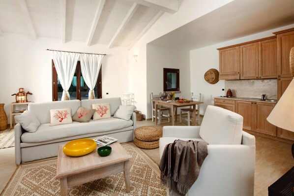 A living room with a sofa, coffee table, and a dining area with a table and chairs. - Holiday Residence Punta Falcone (Santa Teresa di Gallura)