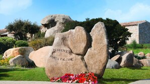 A large rock with "RESIDENCE Punta Falcone" inscribed on it, surrounded by a garden with flowers and greenery. - Holiday Residence Punta Falcone (Santa Teresa di Gallura)