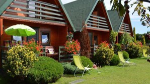 A row of wooden cabins with a well-maintained lawn and outdoor seating areas. - Holiday House in Sarbinowo Near Baltic Beach (Mielno)