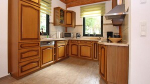 A kitchen with wooden cabinets, a microwave, a stove, and a window with blinds. - Ferienhaus Waldblick in Gohren-lebbin (Goehren-Lebbin)