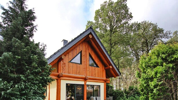 A log cabin with a sloped roof, large windows, and a patio with outdoor seating. - Ferienhaus Waldblick in Gohren-lebbin (Goehren-Lebbin)