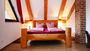 A wooden loft bedroom with a sloped ceiling, exposed beams, and a brick fireplace. - Ferienhaus Waldblick in Gohren-lebbin (Goehren-Lebbin)