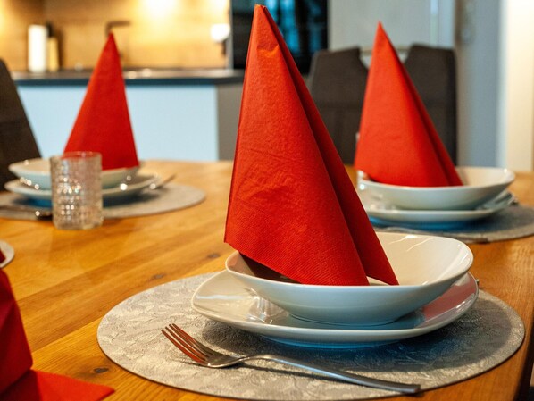 A dining table with red napkins folded into cones, white plates, and silverware on a textured placemat. - Farmhouse in Tobadill With Mountain Views (Tobadill)