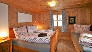 Une chambre confortable, aménagée dans le style d’un chalet, avec des murs et des planchers en bois, un lit avec une literie à motifs, une table de chevet avec une lampe et une fenêtre avec des rideaux.