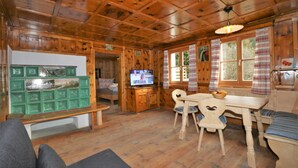 L’intérieur d’un chalet en bois comprend un coin repas, un téléviseur et un meuble vert orné de carreaux décoratifs.