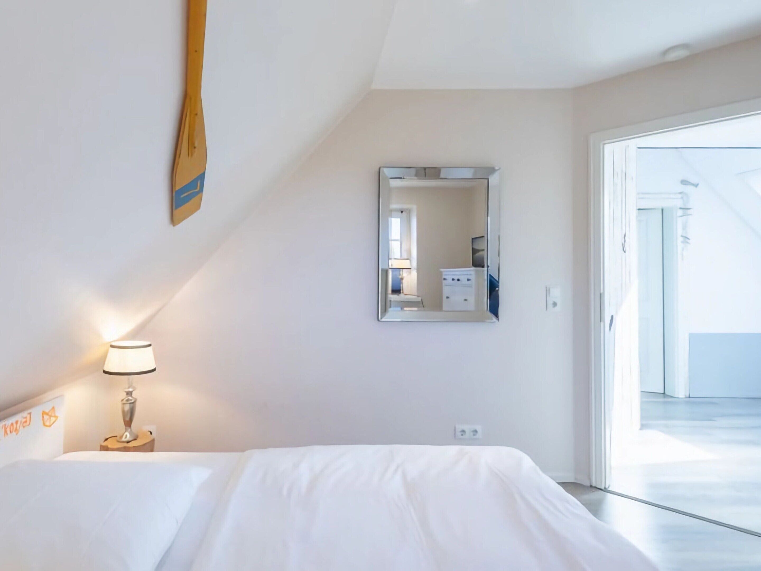Ett hotellrum med en säng, en lampa, en spegel och en dörr som leder ut till en balkong.