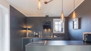 Una cocina moderna con una isla central, iluminación colgante y un ventanal que proporciona luz natural.