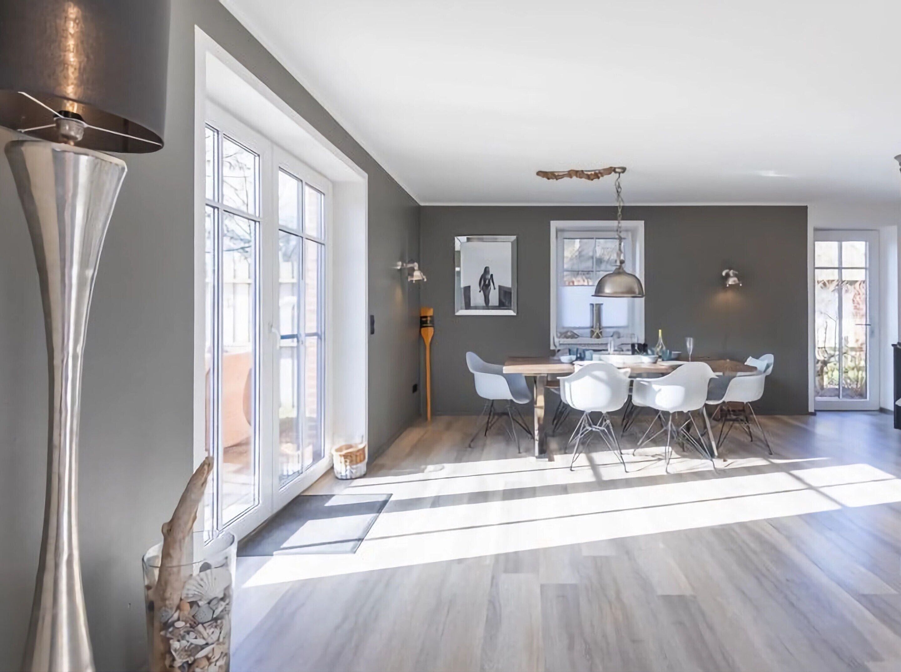 A spacious dining area with a large table and chairs, a pendant light, and a view of the outdoors through large windows.