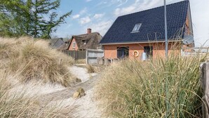 Una casa con techo oscuro y fachada de ladrillo, rodeada de hierba alta y una valla de madera.