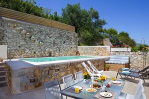A stone pool with a wooden deck, outdoor seating, and a table set for a meal. - Cozy Holiday Home With Pool and Whirlpool in Maheri (Apokoronas)
