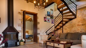 A cozy living room with a stone wall, a fireplace, a staircase, and a sofa. - Cozy Holiday Home With Pool and Whirlpool in Maheri (Apokoronas)
