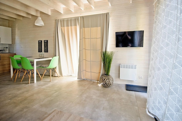 A modern living room with a dining area, a TV mounted on the wall, and a large window with curtains. - Holiday Home Pobierowo Near Baltic Beach (Rewal)