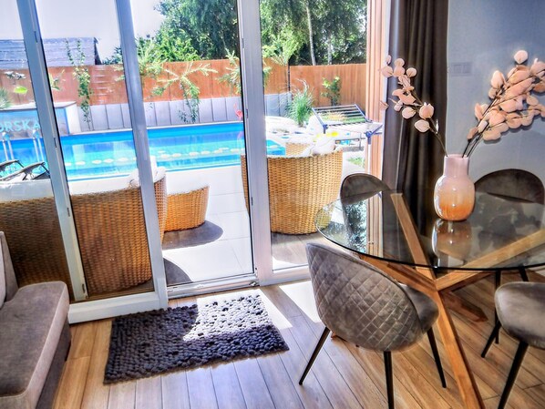 Una sala moderna con una mesa de vidrio, asientos cómodos y vistas a un jardín con piscina.