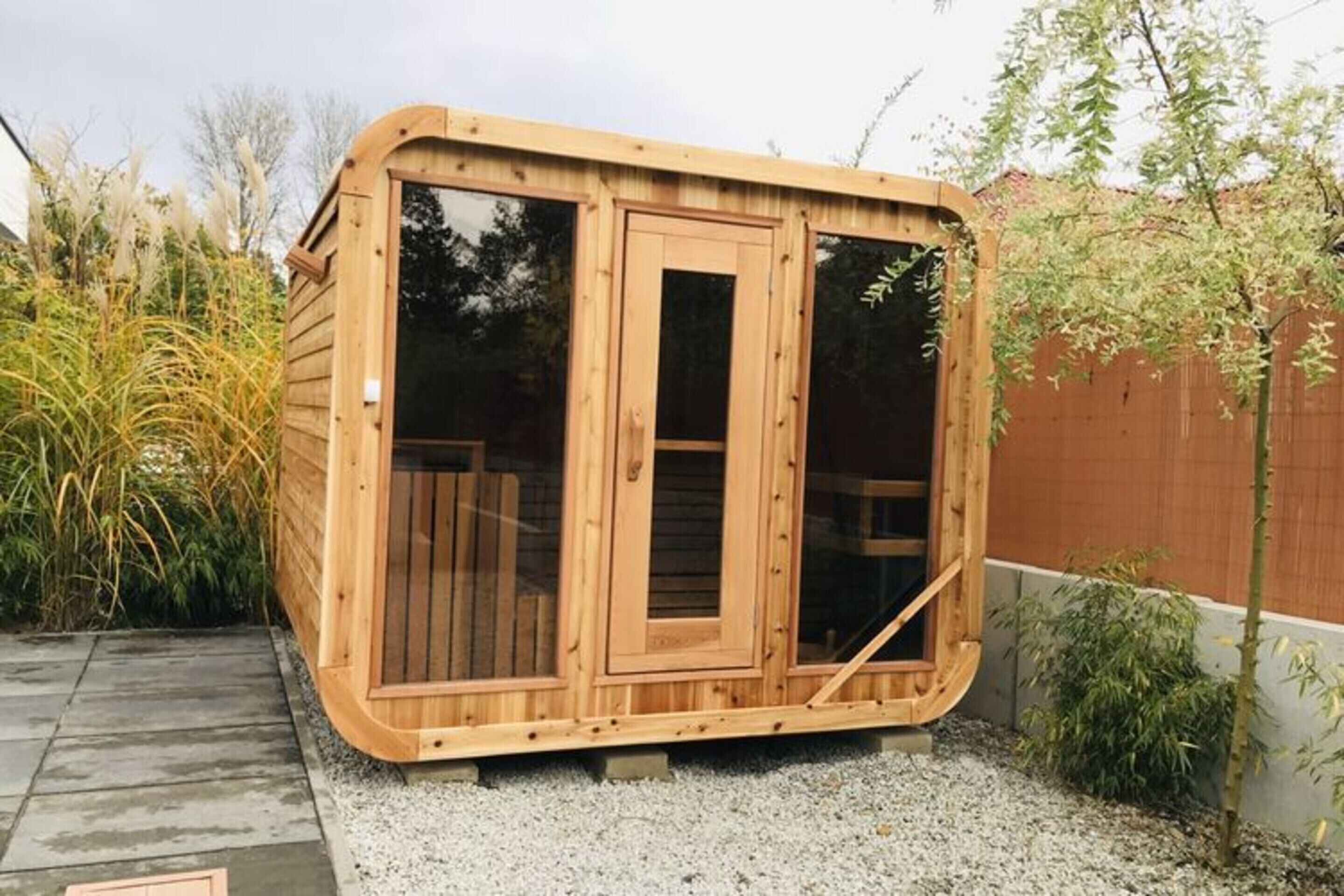 A wooden sauna structure with two large sliding glass doors and a small entrance.