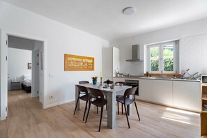 A modern kitchen with white cabinets, a dining table with chairs, and a window providing natural light.