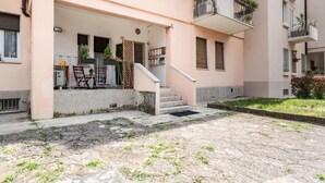 Un edificio residencial con vestíbulo cubierto, mobiliario exterior y una escalera que conduce a los pisos superiores.