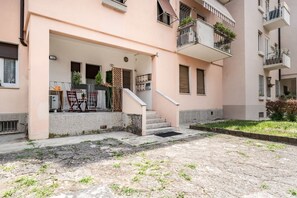A residential building with a covered entrance, outdoor seating, and a staircase leading to the upper floors.
