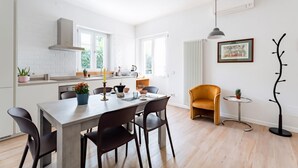 Una cocina moderna con salpicadero de ladrillo blanco, una mesa de comedor con sillas, una pequeña mesa redonda con una planta y un perchero.