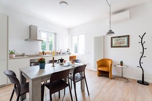 A modern kitchen with white brick backsplash, a dining table with chairs, a small round table with a plant, and a coat rack.