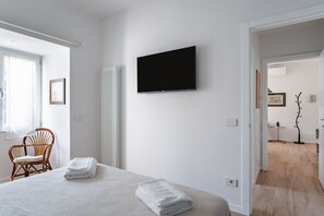 A hotel room with a bed, a television, a chair, and a radiator.