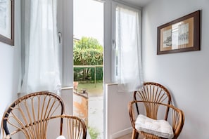 Ein Zimmer mit zwei Korbstühlen, einem gerahmten Bild an der Wand und Blick auf einen Garten durch eine Tür.