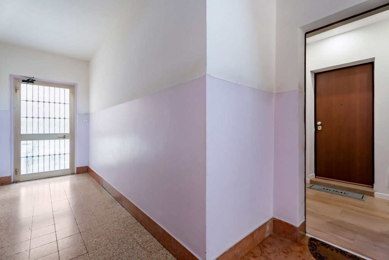 Un pasillo con piso de baldosas, una puerta con reja de metal y una puerta de madera con felpudo.