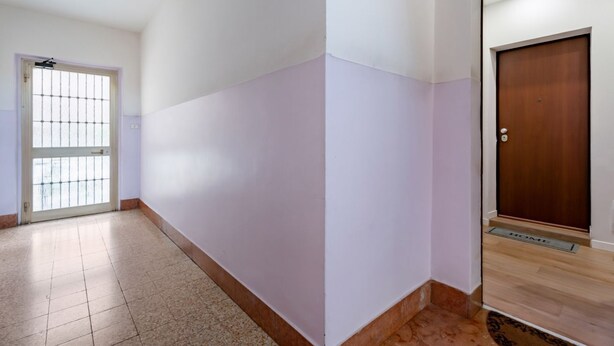 Un pasillo con piso de baldosas, una puerta con reja de metal y una puerta de madera con felpudo.