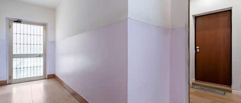 Un pasillo con piso de baldosas, una puerta con reja de metal y una puerta de madera con felpudo.