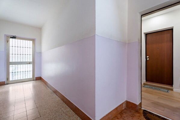 A hallway with a tiled floor, a door with a metal gate, and a wooden door with a doormat.