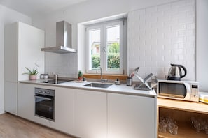 Eine moderne Küche mit weißen Schränken, einem eingebauten Ofen, einer Mikrowelle und einem Fenster mit Blick auf Grünflächen.