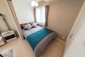 A bedroom with a bed, a heater, a window with curtains, and a door. - UTOPIA 101 (Sapporo)