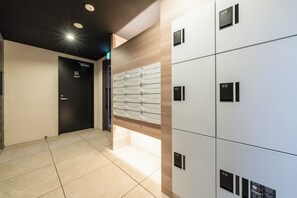 A hotel lobby with a modern design, featuring a reception desk, a black door with a sign, and a row of numbered lockers. - UTOPIA 101 (Sapporo)