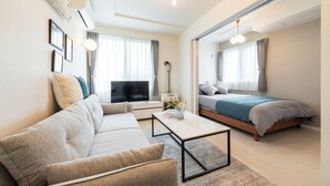 A modern, well-lit living room with a sofa, coffee table, and a bed with a blue bedspread. - UTOPIA 101 (Sapporo)