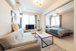 Una sala de estar moderna y luminosa con un sofá, una mesa de centro y una cama con colcha azul.