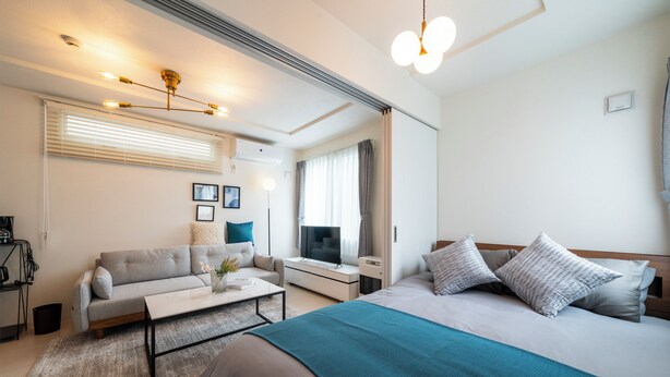 A modern hotel room with a large bed, a sofa, a coffee table, a TV, and a desk. - UTOPIA 101 (Sapporo)
