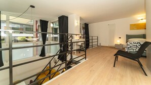 A modern bedroom with a bed, a chair, a desk, and a staircase. - GuestHost - Galaxy Lofts - Appt Jupiter x4 (Torino)