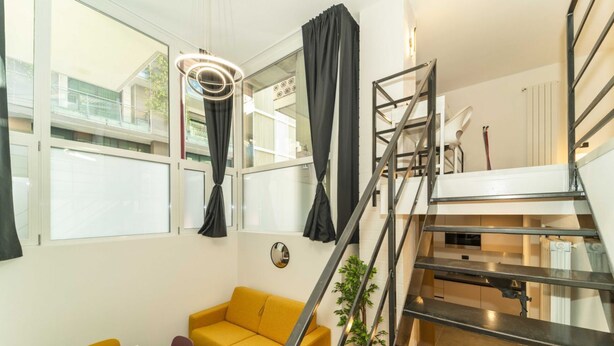 A modern interior with a yellow sofa, a dining table, a staircase, and a view of the outside. - GuestHost - Galaxy Lofts - Appt Jupiter x4 (Torino)
